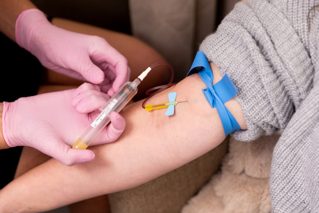 Close up of gloved hands drawing blood from an outstretched arm to perform testing for hormone replacement therapy near Storm Lake.