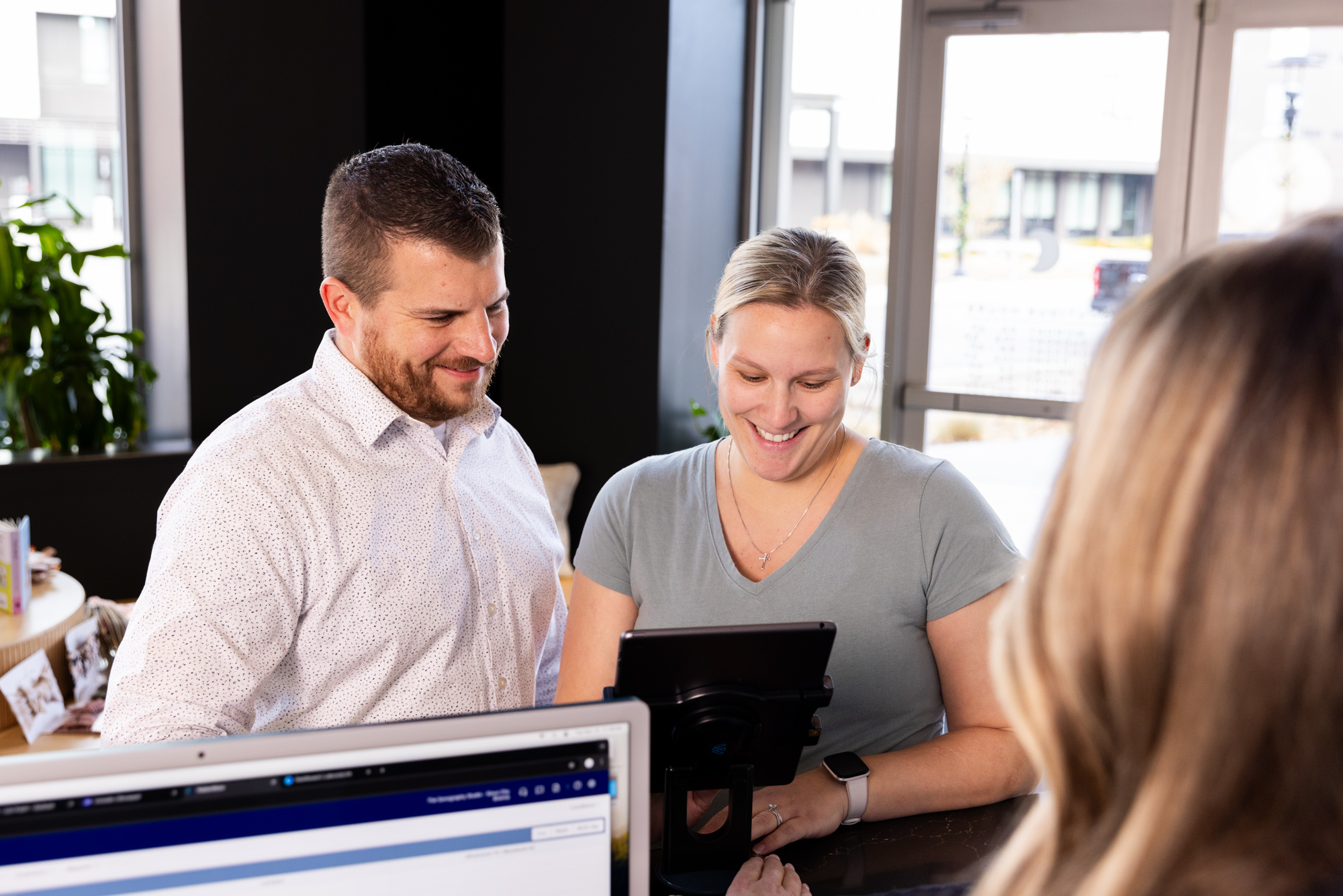 A man and woman smiling while filling out paperwork on a tablet at the front desk before a treatment for Vaginal Rejuvenation Near Omaha.